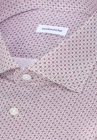 Chemise à col avec petit motif géométrique marron et blanc et boutons blancs, montrant une étiquette avec le texte « seidensticker » à l'intérieur du col.