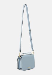 Vaaleansininen nahkalaukku, jossa on jäsennelty muotoilu, kultaiset metalliosat, irrotettava hihna ja yläkahva. Laukussa on vetoketjutasku.