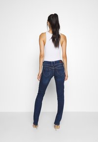 Džíny s úzkým střihem v tmavě modrém odstínu s jemným vyblednutím, s kapsami na zadní straně zdobenými prošíváním a koženou značkovou štítkem v pase.