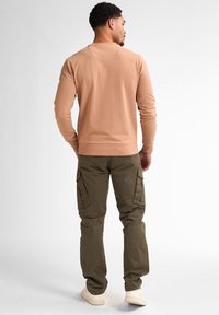 Felpa marrone chiaro con maniche lunghe, scollo rotondo e orlo a coste, abbinata a pantaloni cargo verde oliva con tasche laterali.