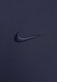 Tissu bleu foncé avec un logo Nike swoosh brodé en relief avec un fil bleu foncé assorti.