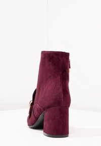 Burgundy mocka ankelsko med klack, med en sidokut och metallisk detalj. Slät yta med rund tå.