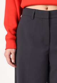 Dark gray dress pants featuring a smooth texture, front pleats, and a fitted waistband. Hand placed on the side for scale.