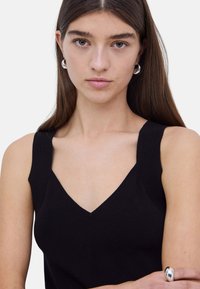 Top de punto negro con escote en V y tirantes anchos. Presenta un diseño ajustado y una textura suave. Estilo simple y minimalista.
