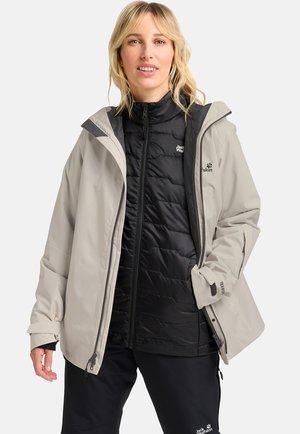 Light grey waterproof jacket over a black padded vest, both with zippers and logo accents, featuring wide sleeves and a relaxed fit.