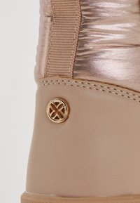 Knee-high saapad, millel on metallik roosa peals ja beež nahast alus. Omab kuldset ümmargust aktsenti ja tekstureeritud elastset paneeli.