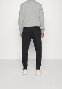 Gray sweatshirt, black joggers with a back pocket, smooth texture, fitted design, paired with white sneakers featuring brown accents.
