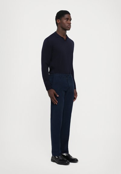 Navy long-sleeve polo and matching trousers, both in smooth fabric. Black shoes, tailored fit, subtle texture in the pants. Simple design.