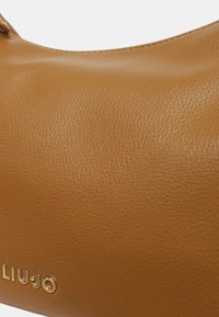 Borsa a spalla in pelle marrone con texture, caratterizzata da una finitura liscia, logo del marchio impresso e dettagli di cuciture superiori discreti.