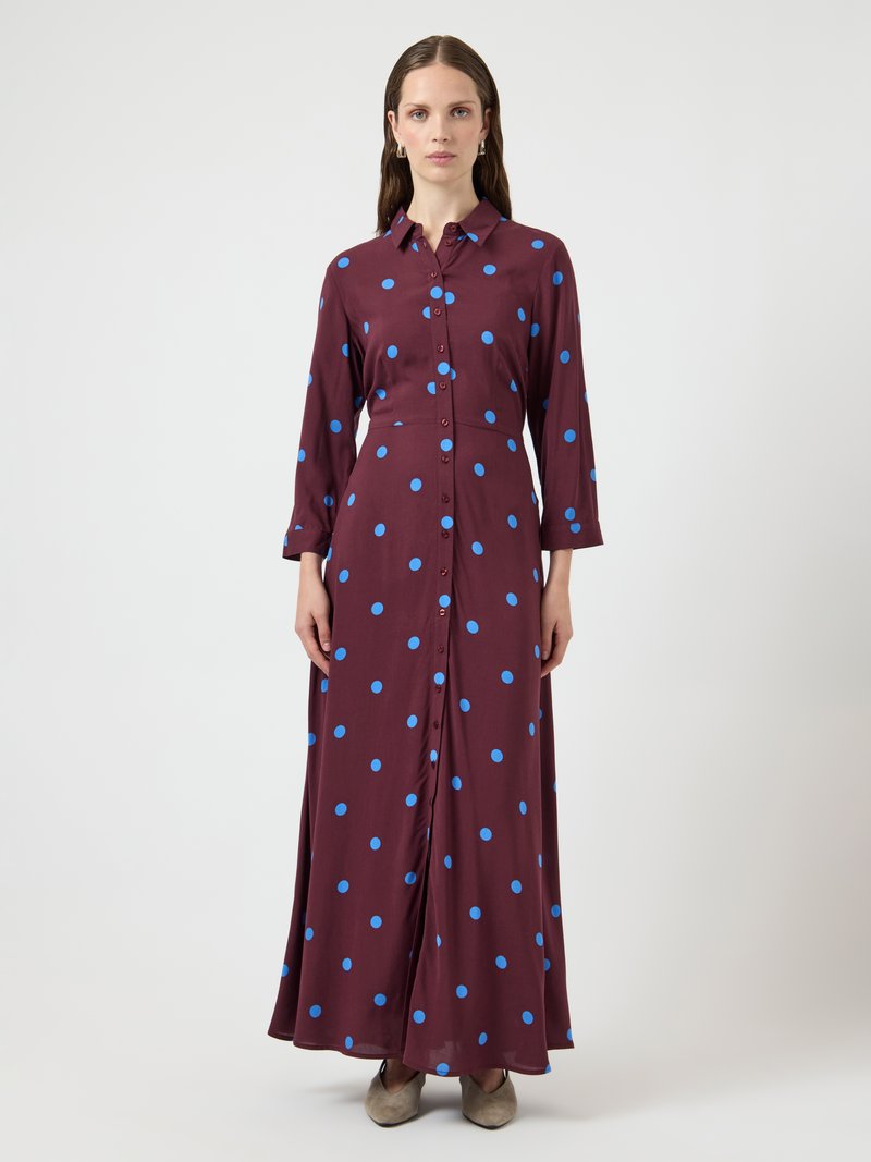 Maxikleid in Weinrot mit blauen Polka Dots, langen Ärmeln und tailliertem Schnitt. Hergestellt aus einem glatten, leichten Stoff.