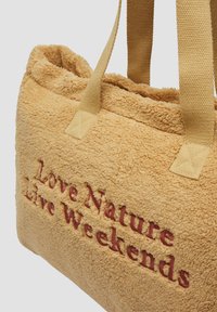 Torba tote o fakturze przypominającej trawę, z pluszowego materiału, z haftowanym napisem "Kochaj naturę, żyj weekendami" w burgundowym kolorze. Posiada plecione ramiączka.