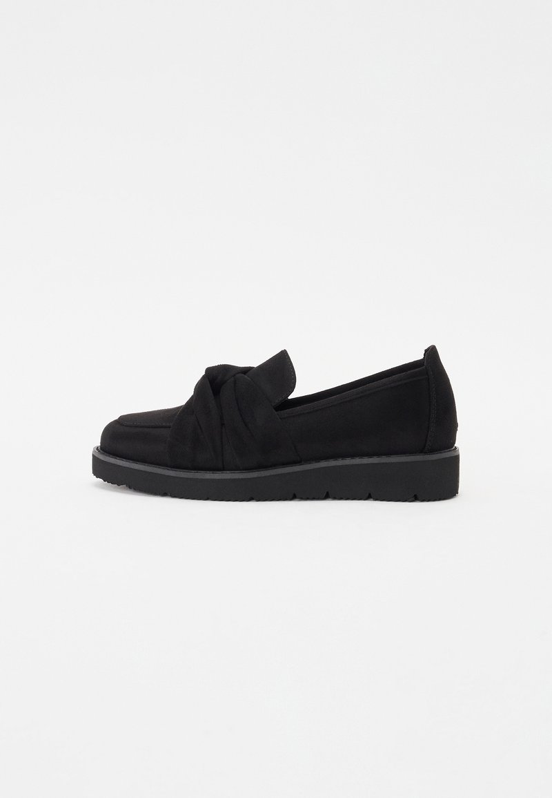 Mocassin plat noir avec une semelle épaisse et un détail en tissu torsadé sur le dessus, présenté en profil latéral sur fond blanc.
