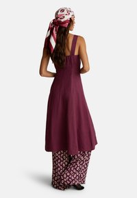 Vestido sin mangas color marrón con un diseño fluido. Tejido texturizado que se extiende hasta unos pantalones estampados con motivos de hojas blancas. Acompañado de una bufanda estampada.