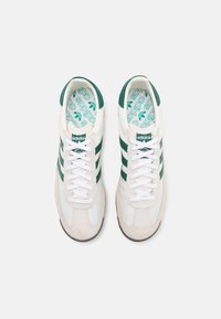 Zapatillas deportivas blancas con rayas verdes, punta de gamuza y suelas de goma texturizadas. Con una plantilla con un patrón y acentos de logo.