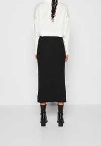 Černá žebrovaná midi sukně se rovnou siluetou, texturovaná látka, nošena s černými podpatkovými botami a bílou košilí.