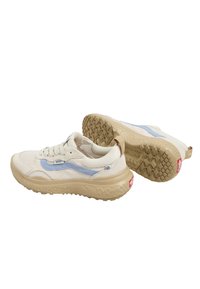 Vaaleanbeige verkkomateriaalista valmistetut lenkkitossut, joissa on vaaleansiniset yksityiskohdat. Tossuissa on teksturoitu vaaleanbeige pohja ja pyöreä muoto. Brändäys näkyy sivussa ja kielen kohdalla.