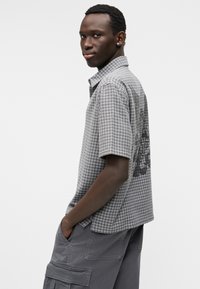 Γκρι κοντομάνικο πουκάμισο με καρό σχέδιο και γραφικό σχέδιο στην πλάτη; συνδυασμένο με γκρι cargo σορτς.