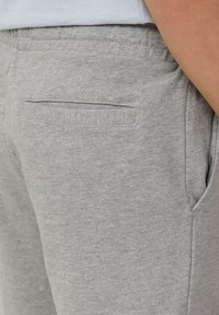 Grijze joggingsbroek met een zachte textuur, elastische tailleband en een achterzak met een vlakke opening. Het materiaal lijkt een katoenmix te zijn.