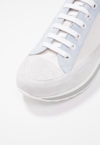 Grå och ljusblå sneaker med en mjuk mocka tåhätta, lädersidor och vita snörningar. Har en texturerad sula och minimala designelement.