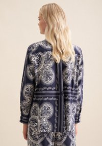 Blusa a fantasia navy con design paisley, maniche lunghe e vestibilità rilassata. Il tessuto appare liscio con lucentezza e presenta un polsino con bottoni.