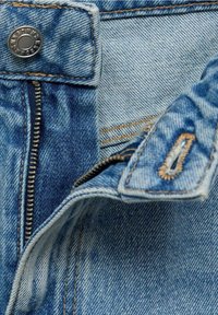 Jean en denim bleu avec une fermeture éclair métallique partiellement ouverte et un bouton argenté à la taille montrant des coutures détaillées.