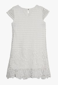 Vit klänning med texturerade cirkulära detaljer över bysten, spetsdekoration vid fållen och korta ärmar. Nyckelhålsöppning i ryggen.