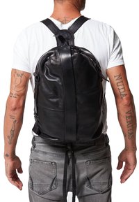 Mochila de cuero negro con correas ajustables, forma redondeada, textura suave y cierre central con cremallera. Presenta un diseño minimalista.