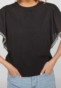 Černé tričko s krátkými, průhlednými, nafouklými rukávy, zdobené bílou krajkou. Minimalistický design s kulatým výstřihem a volným střihem.