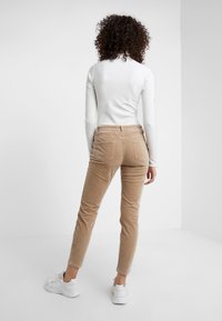 Pantalones de pana beige con un corte ajustado, cuentan con bolsillos traseros y una pierna ligeramente ajustada, combinados con zapatillas blancas y una camiseta ajustada.