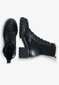 Černé kotníkové boty vyrobené z jemné kůže a uhlazené kůže. Mají robustní podpatek, kulatou špičku a šněrování se kovovými dírkami. Texturovaná podrážka.