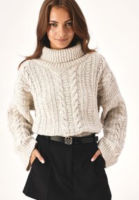 Suéter de punto grueso con diseño de cuello vuelto, que presenta puños acanalados y un ajuste holgado, combinado con pantalones cortos negros de talle alto.