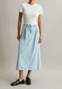 Ljusblå denim maxi kjol med rak skärning, hög midja, detaljer med fram söm, kombinerad med en figurnära vit kortärmad skjorta och svarta skor.