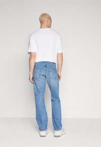 Lichtblauwe jeans met een relaxte pasvorm en rechte pijpen, voorzien van achterzakken en een middelhoge taille, gecombineerd met een wit shirt met korte mouwen.