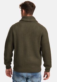 Sweter w oliwkowym odcieniu z dzianiny, z wysokim kołnierzem, teksturowanym materiałem i ściągaczami. Stylizacja z casualowymi dżinsami.