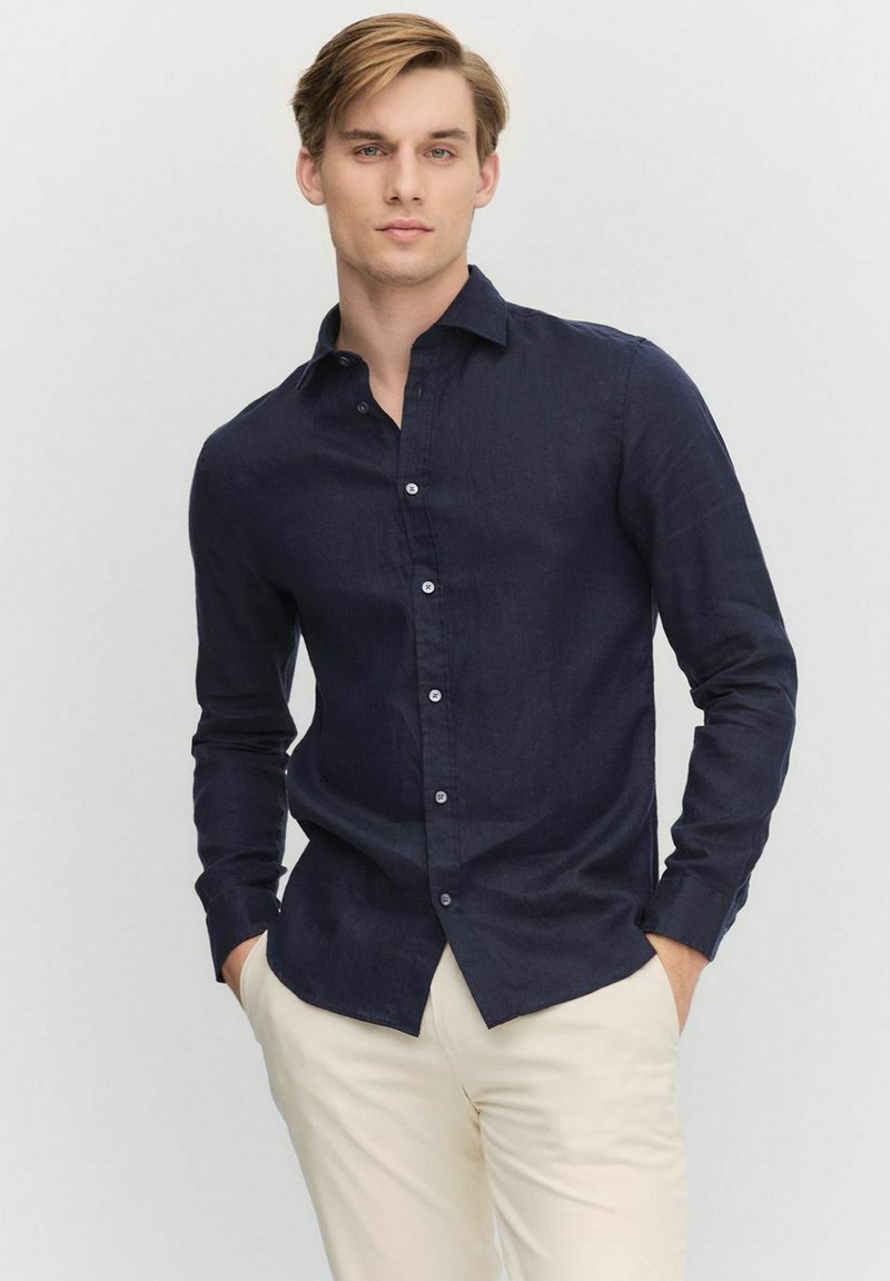 Marineblauw overhemd met knopen van lichtgewicht linnen, met een klassieke kraag, lange mouwen en een slim fit, gecombineerd met lichtgekleurde broeken.
