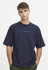 Marineblå oversized t-skjorte laget av bomull, med korte ermer og rund hals, med "Casual" trykt i lys grønn.