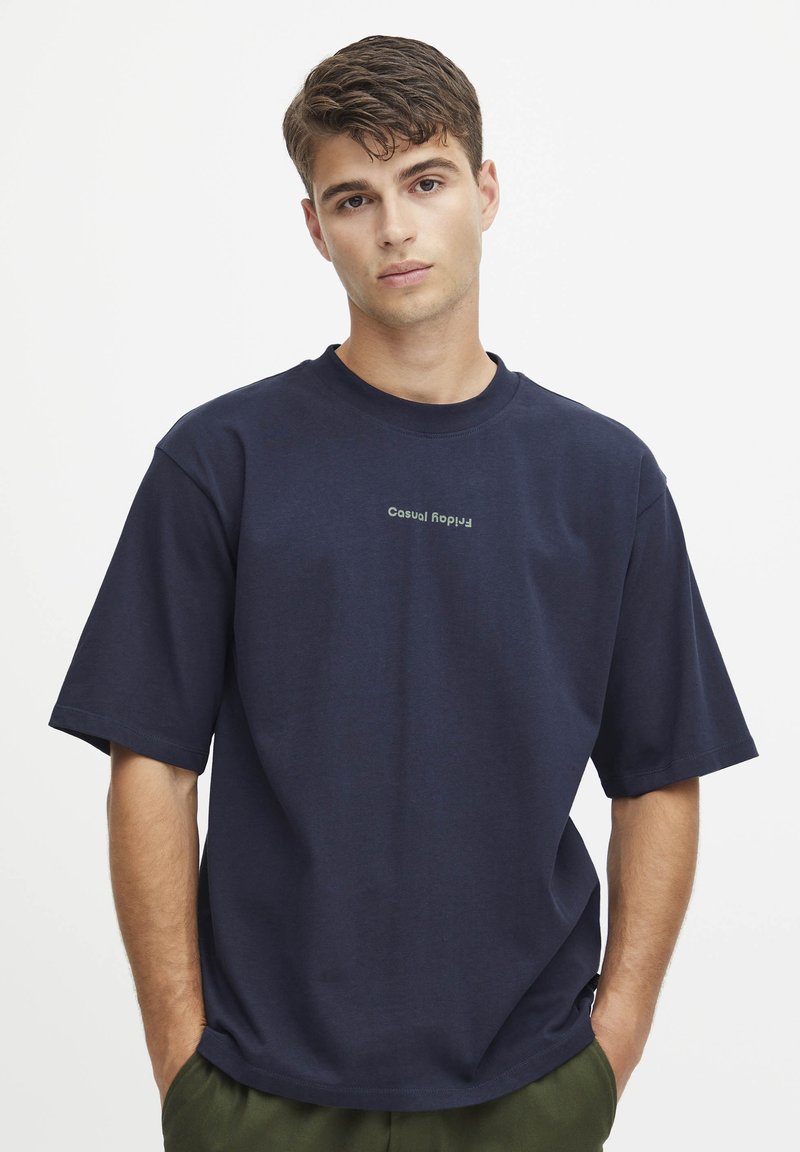 Marineblå oversized t-skjorte laget av bomull, med korte ermer og rund hals, med "Casual" trykt i lys grønn.
