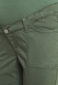 Gröna tygbyxor med slim fit, som har framfickor och detaljerad sömnad. Materialet verkar mjukt och lätt texturerat.