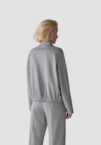 Gray, textured knit jacket with a high collar, elastic waistband, long sleeves, and matching pants, shown from the back against a plain background.