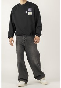 Felpa nera a maniche lunghe con colletto tondo, caratterizzata da toppe grafiche colorate, abbinata a jeans grigi scuri a vestibilità ampia con silhouette rilassata.