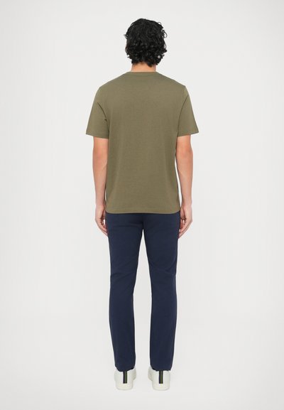 Tricou verde măsliniu cu mâneci scurte, guler rotund, asortat cu pantaloni bleumarin. Materialul pare neted; pantofii sunt deschiși la culoare, cu accente multicolore.