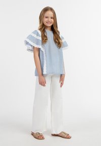 Lys blå stribet top med hvid blondekant, parret med hvide brede bukser og guld sandaler med remme. Simpelt og casual design.