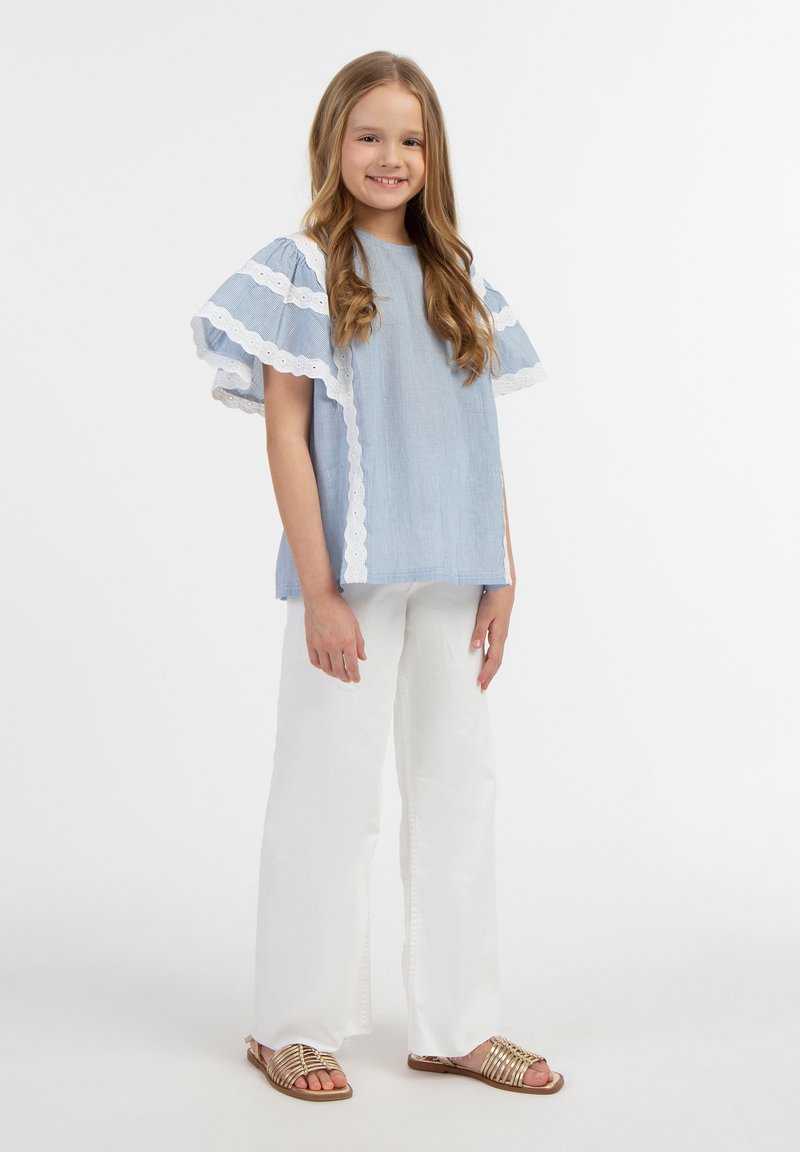 Lys blå stribet top med hvid blondekant, parret med hvide brede bukser og guld sandaler med remme. Simpelt og casual design.