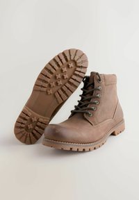 Bruna läderankelboots med rund tå, snörning framtill, texturerad gummisula och kontrasterande sömmar.