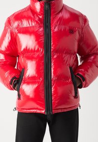 Rote Steppjacke mit glänzendem Finish, Reißverschluss, verstellbaren Bündchen und Seitentaschen. Auf der linken Brust befindet sich ein schwarzes Logo.