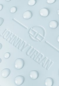 Ljusblå strukturerad yta med upphöjda cirkulära droppar och präglad "JOHNNY URBAN"-logotyp, som betonar dess taktila design och varumärke.