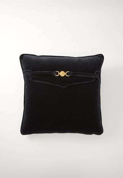Černý sametový čtvercový polštář s zaoblenými okraji, který na přední straně má zlatý kulatý akcent a detail s páskem. Měkká textura.