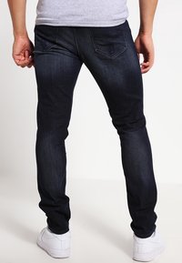 Tmavě modré džíny se slim střihem, s zadními kapsami a jemným prošitím. Kombinované s bílými teniskami.