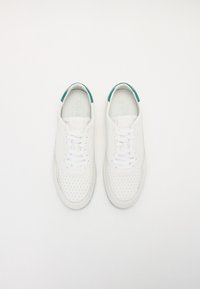 Hvite lær sneakers med perforert tå, hvite snøringer og grønn detalj på hælen. Flat såle og minimalistisk design.
