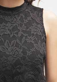 Top in pizzo nero con scollatura alta, caratterizzato da motivi floreali e un design in rete testurizzata, maniche corte e una silhouette aderente.